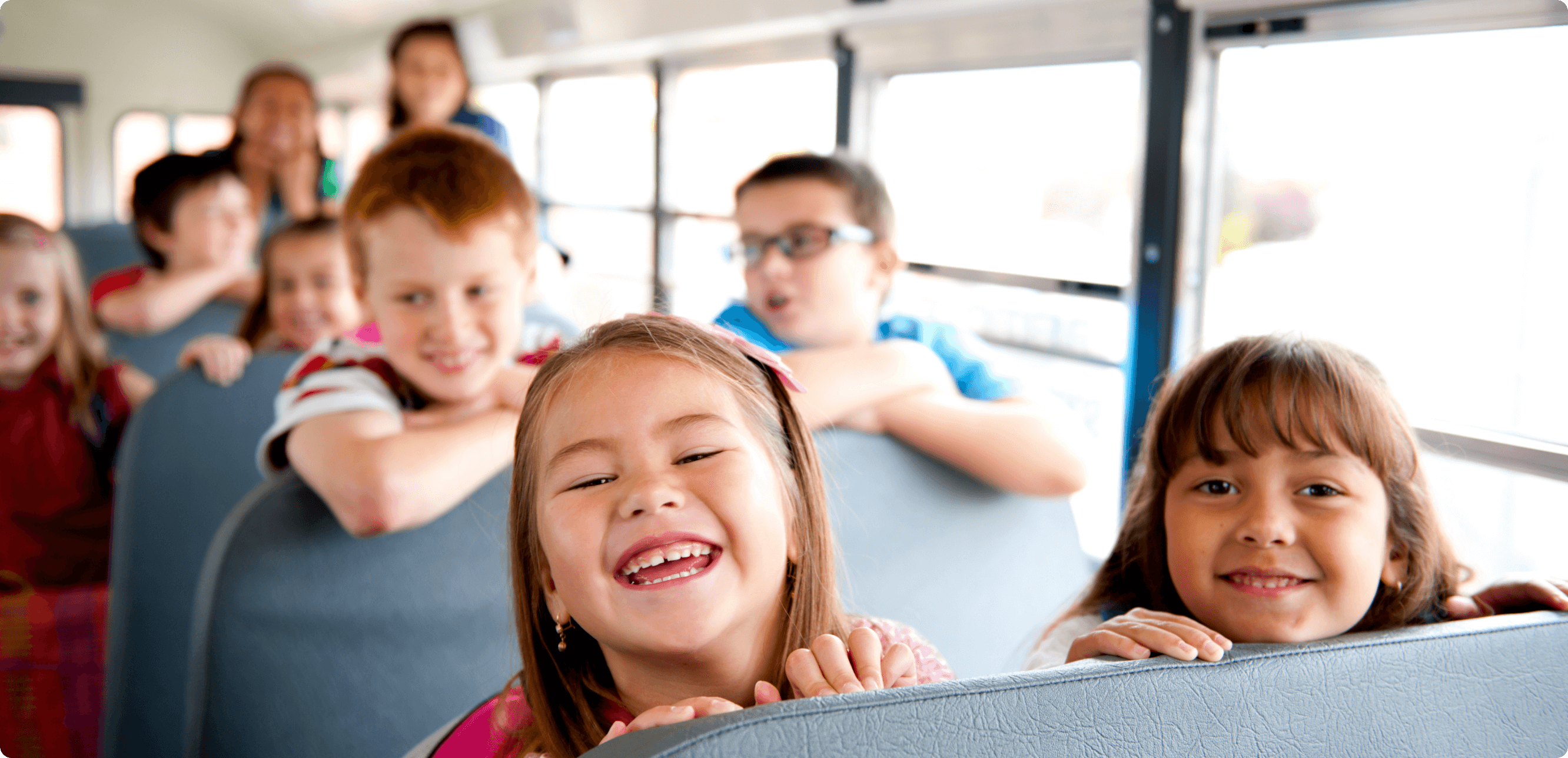 a group of young school children sitting on a school bus interior, all smiling