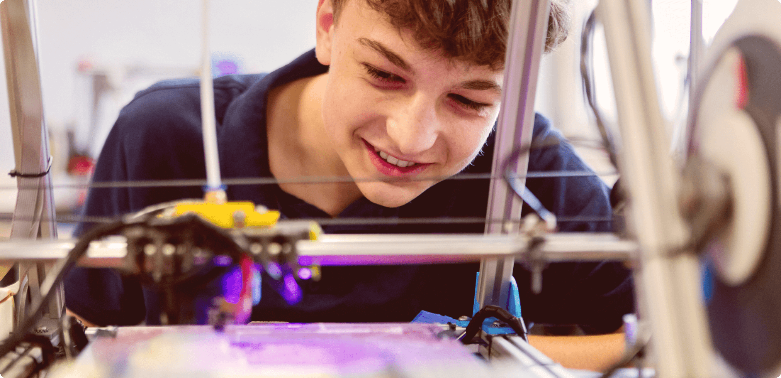 a teenage boy looking over a 3D printer mid-print
