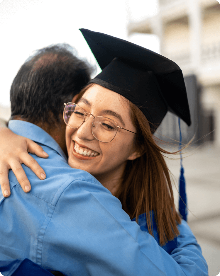 an older teenage wearing glasses and a graduation cap giving a hug to an older male figure