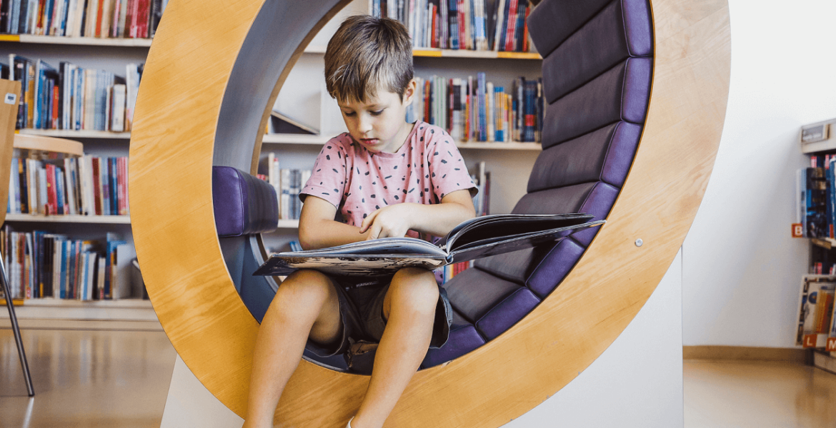 A young boy sitting in a round chair reading a picture book