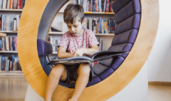 A young boy sitting in a round chair reading a picture book