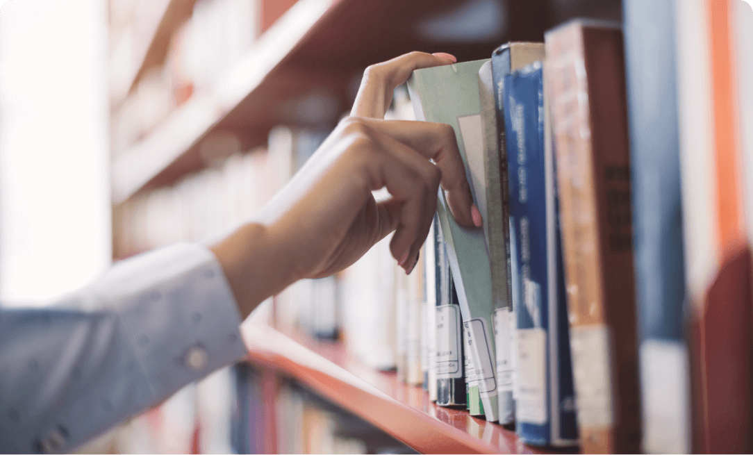 close up of the hand of a dark skinned girl picking out a book from a library shelf