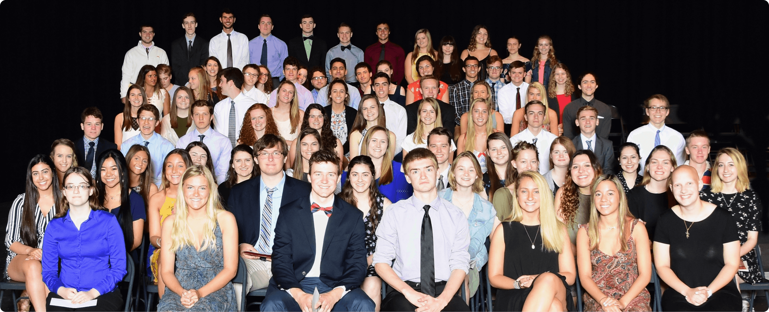 A photo of approximately 50 or so older students, either late high school or early college, sitting and smiling at the camera.