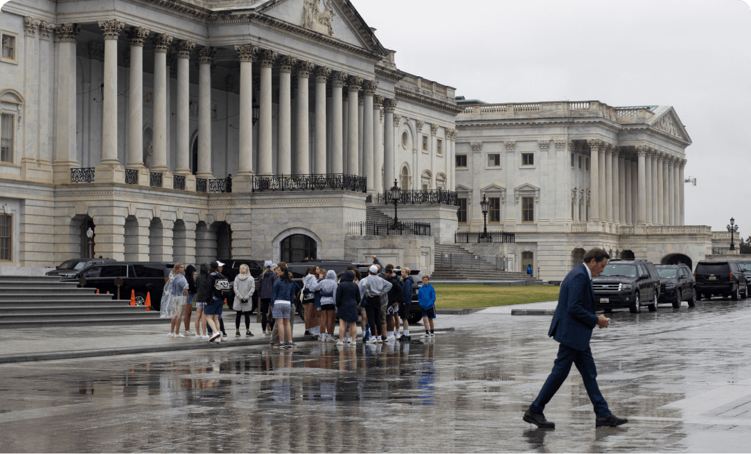 a group of students outside a government building in washington dc. It is rainy and a man in a suit is walking in the foreground