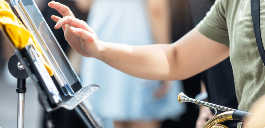close up image of a young student's hand hovering over a tablet on a music stand. The student is holding a french horn