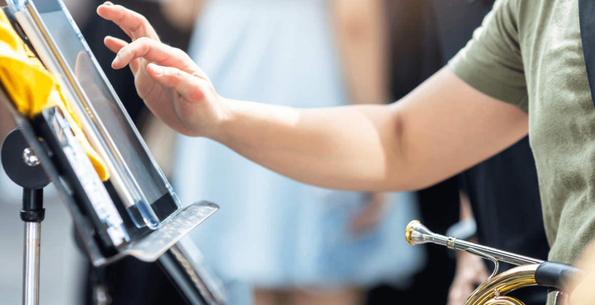 close up image of a young student's hand hovering over a tablet on a music stand. The student is holding a french horn